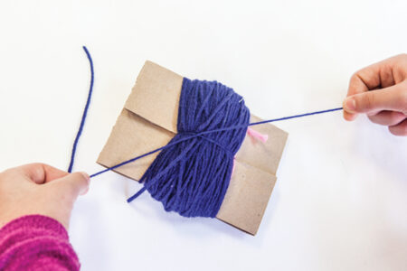 person tying a string of yarn around the middle of yarn wrapped around cardboard